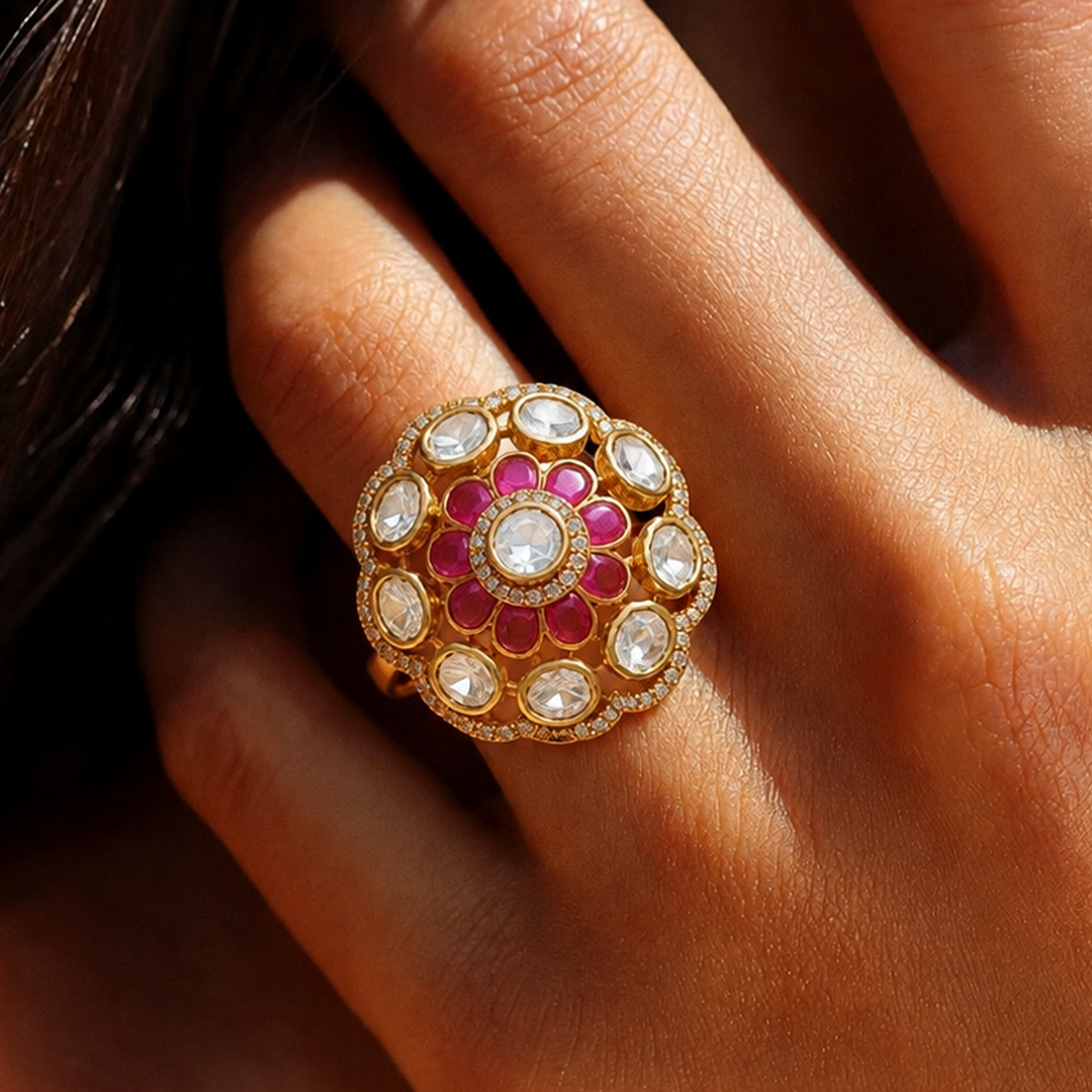 A close-up of a hand wearing an ornate gold ring with a floral design featuring pink stones and clear round stones.